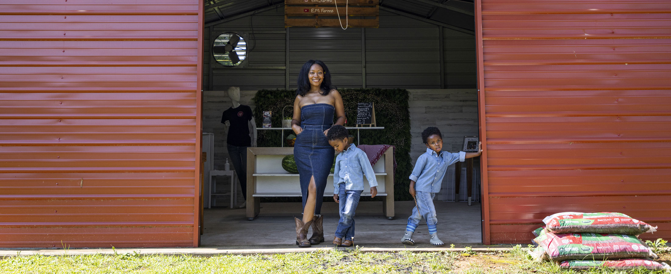 Twin boys standing with their mom in front of a red barn.